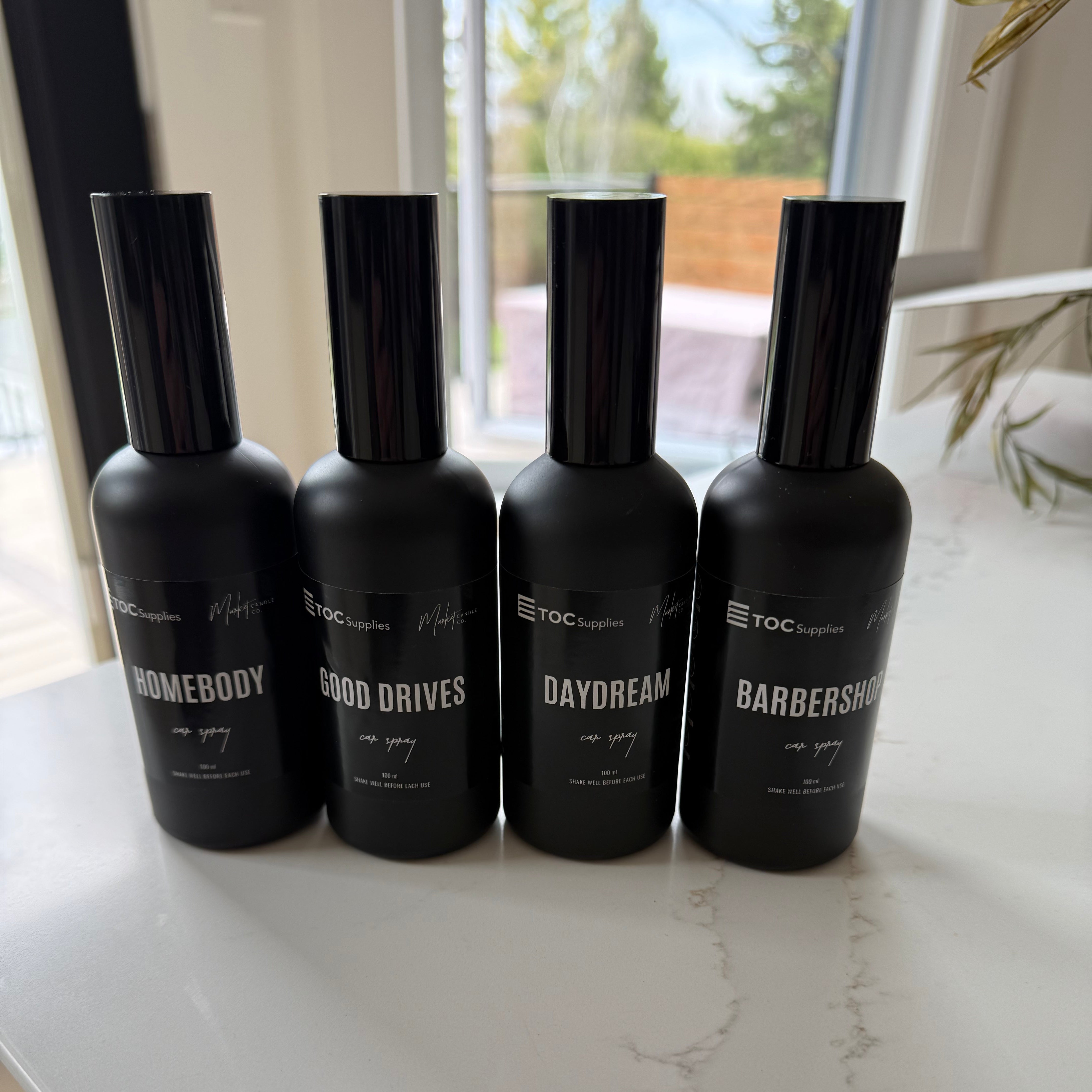 Four black bottles with labels on a white surface near a window